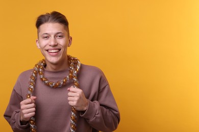 Photo of Happy young man with tinsel on orange background, space for text