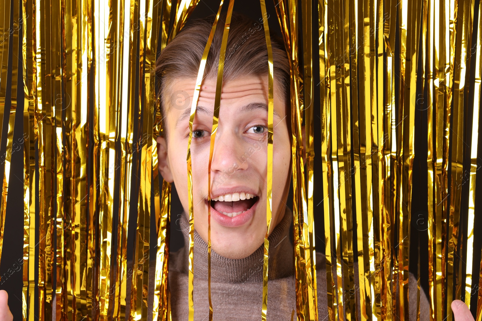 Photo of Happy young man near golden foil curtain against dark background