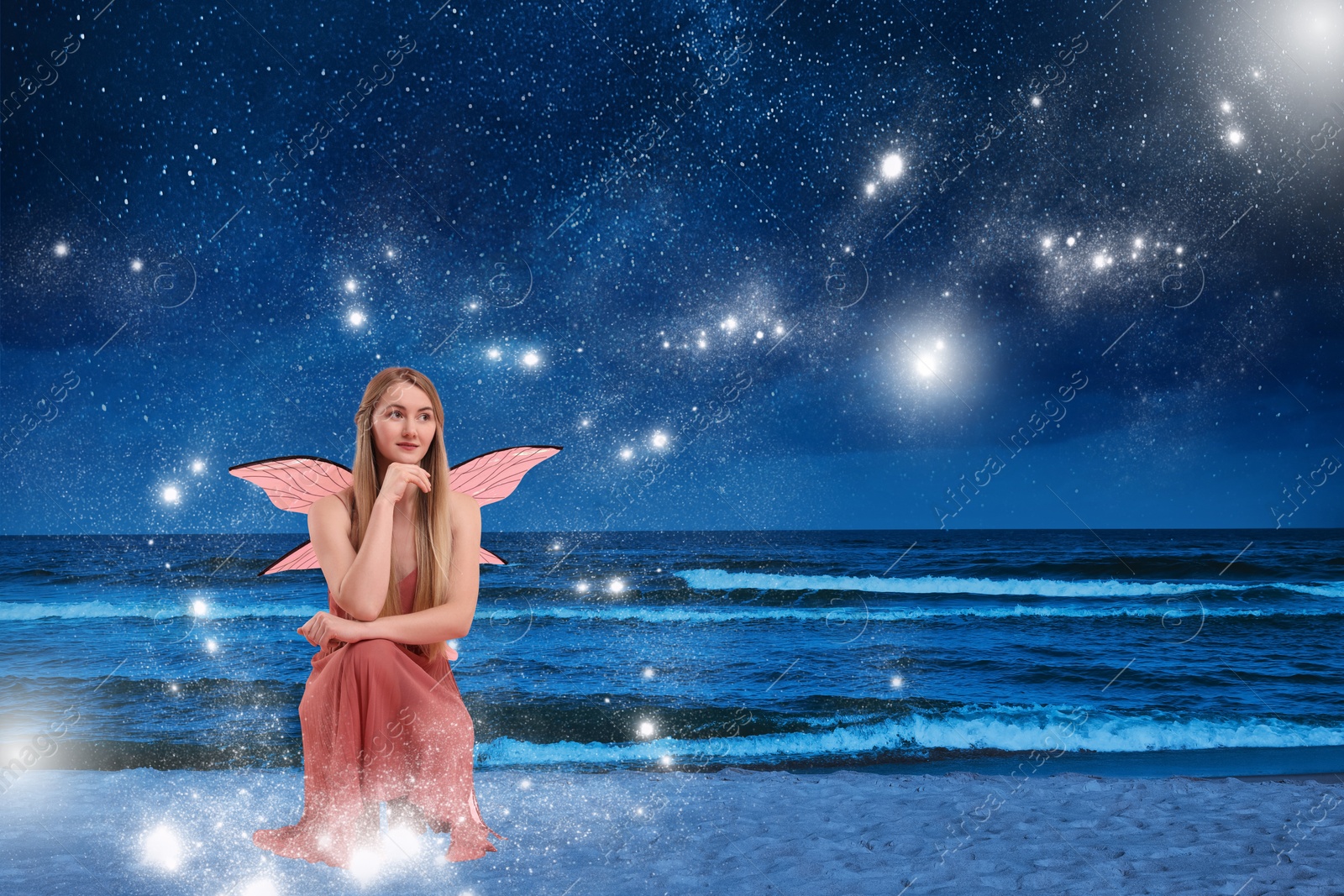 Image of Enchanting fairy on seashore, magic lights gathering around her. Beautiful girl with wings