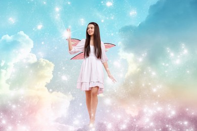 Image of Ethereal fairy casting magic lights while walking among fluffy clouds in colorful sky. Beautiful girl with wings near rainbow