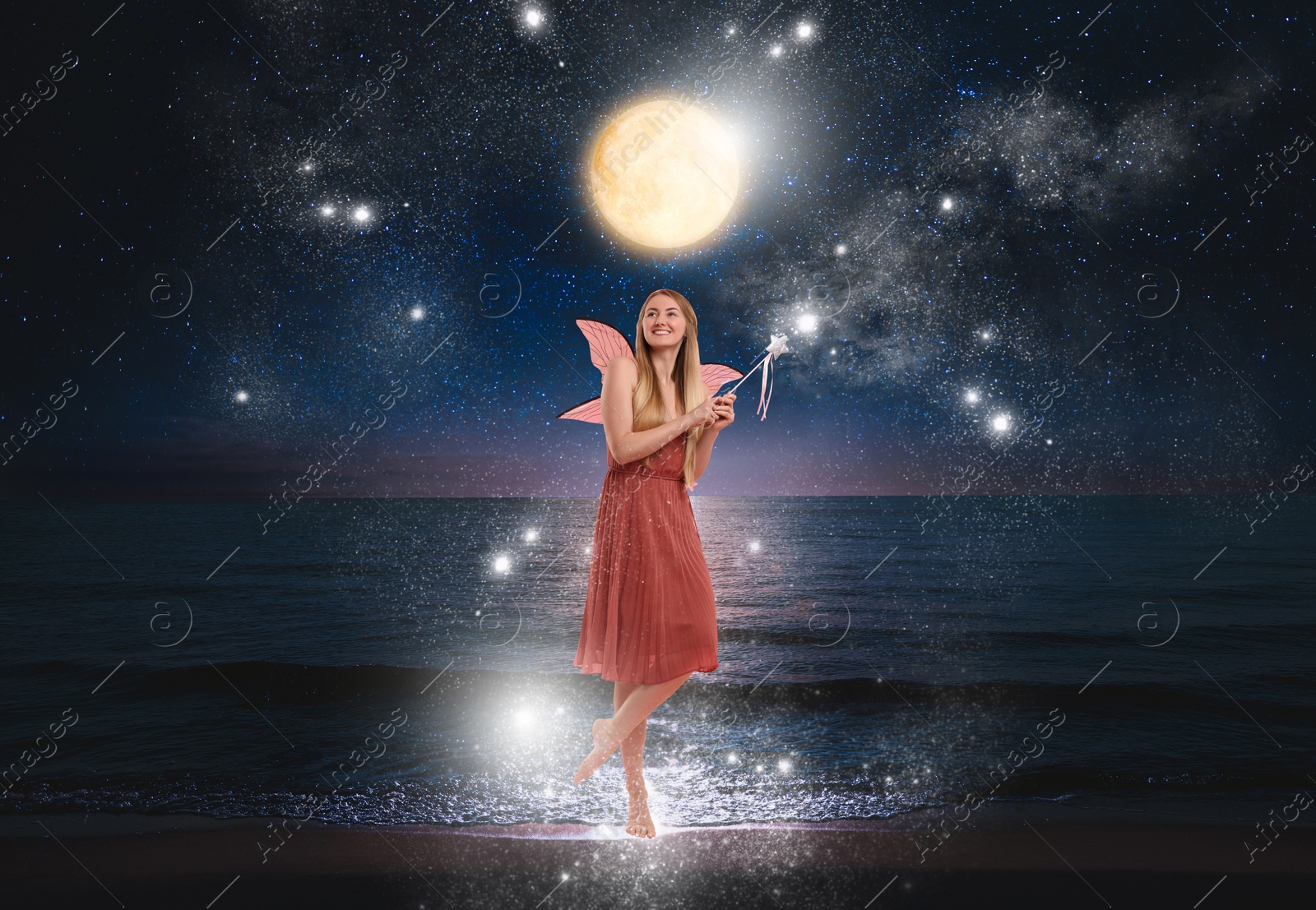 Image of Enchanting fairy igniting magic lights on seashore under full moon. Beautiful girl with wings