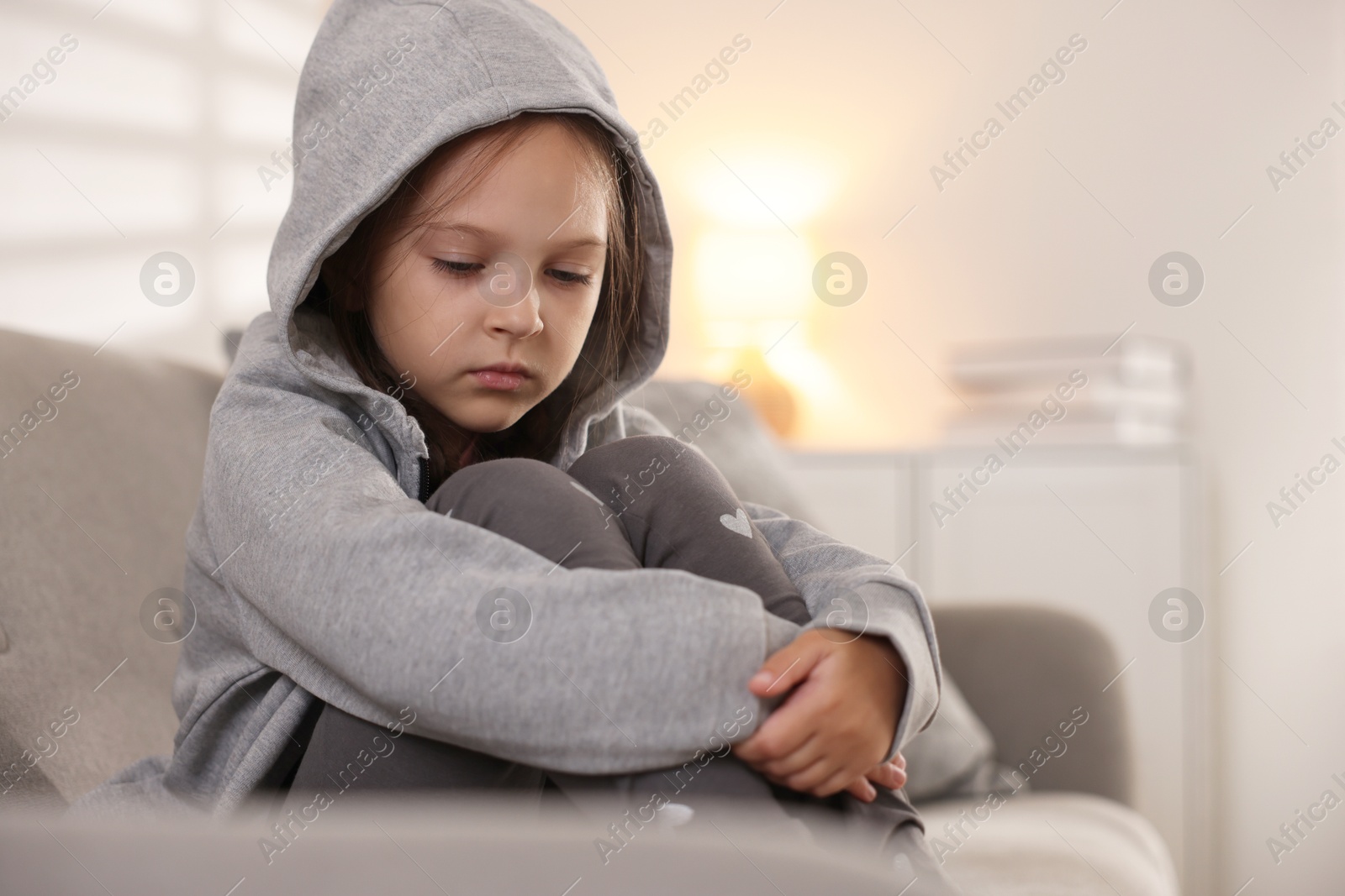 Photo of Orphanage concept. Sad girl sitting on sofa indoors