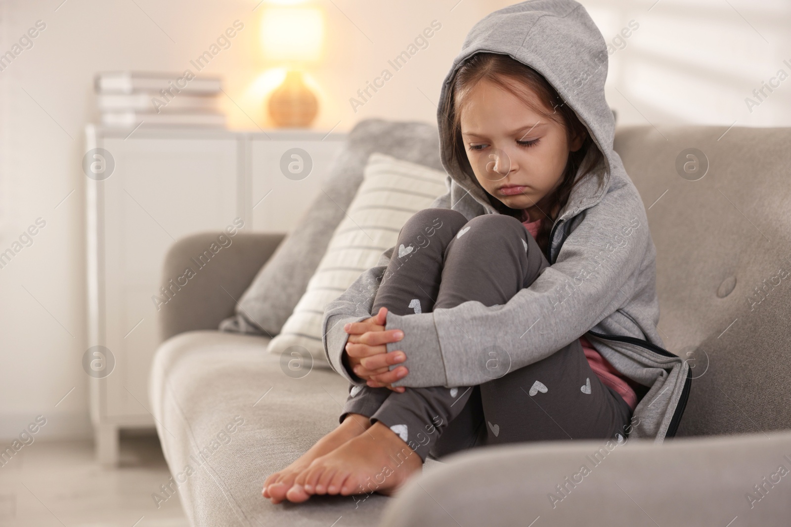 Photo of Orphanage concept. Sad girl sitting on sofa indoors