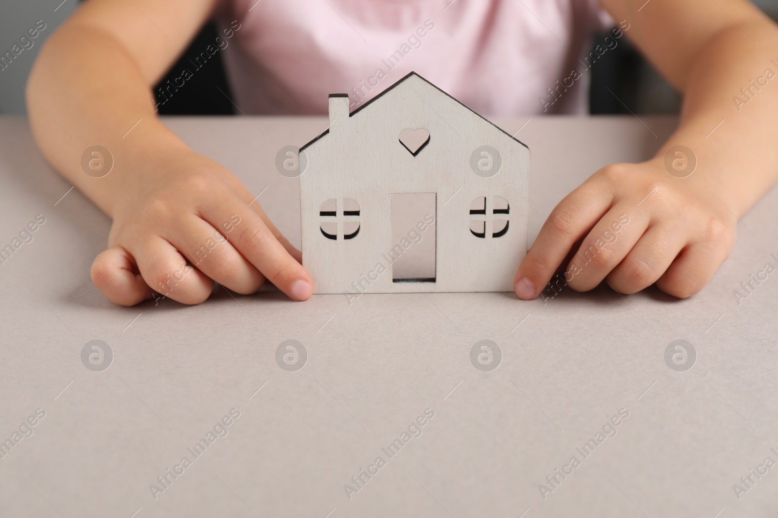 Photo of Adoption concept. Kid with cutout of house at light grey table, closeup