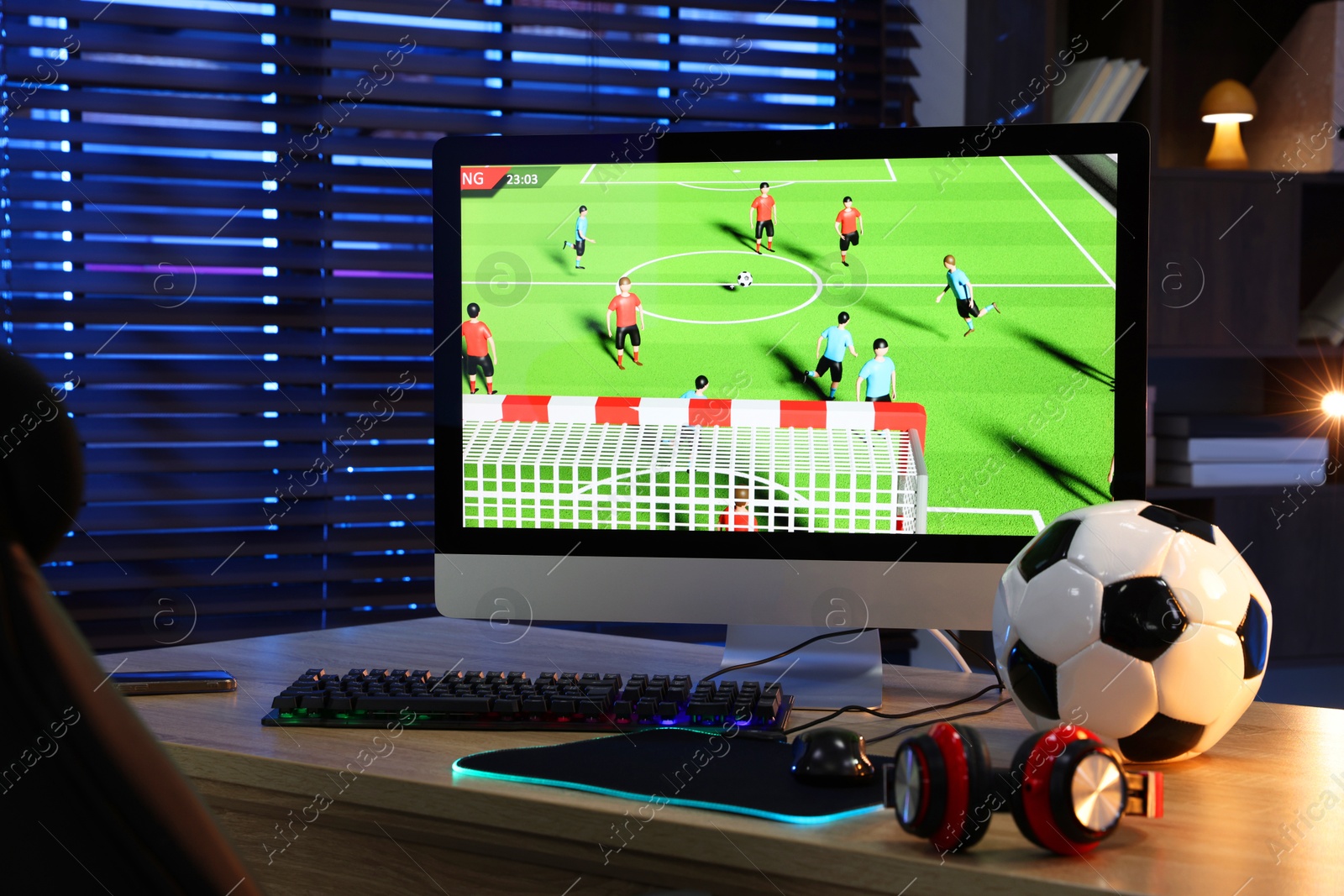 Photo of Computer keyboard, monitor, soccer ball, headphones and mouse on table indoors