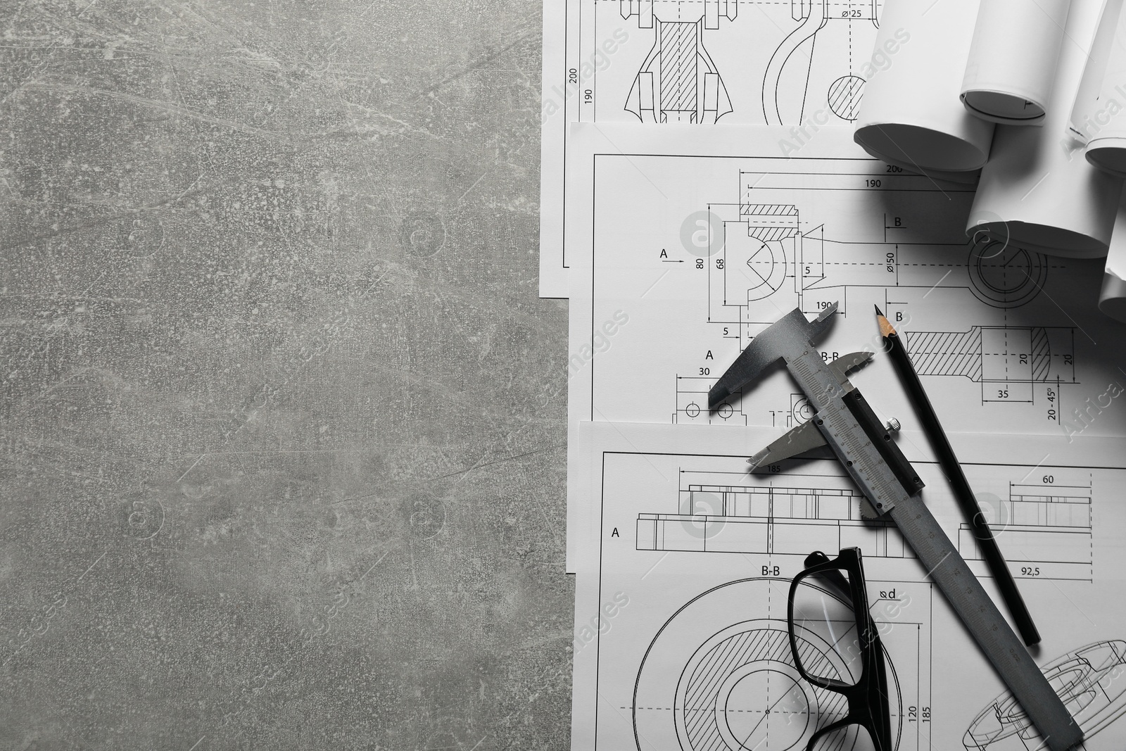 Photo of Different engineering drawings, vernier caliper, pencil and glasses on gray textured table, top view. Space for text