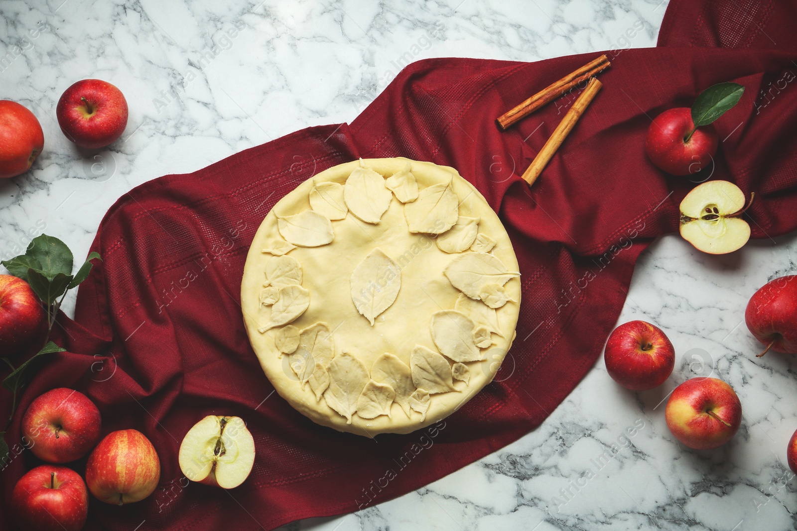 Photo of Raw homemade pie, apples and cinnamon sticks on white marble table, flat lay