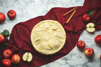 Photo of Raw homemade pie, apples and cinnamon sticks on white marble table, flat lay