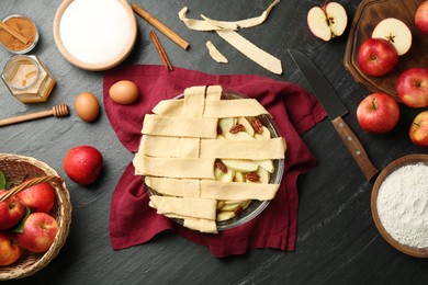 Photo of Flat lay composition with raw homemade apple pie and ingredients on dark textured table