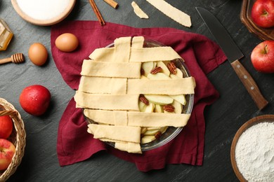 Photo of Flat lay composition with raw homemade apple pie and ingredients on dark textured table