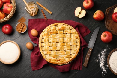 Photo of Flat lay composition with tasty homemade apple pie and ingredients on dark textured table