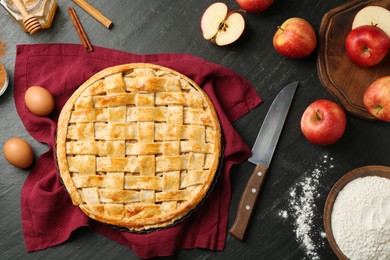 Photo of Flat lay composition with tasty homemade apple pie and ingredients on dark textured table