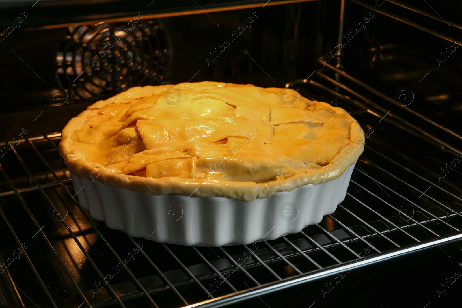 Photo of Baking dish with raw homemade apple pie in oven, closeup