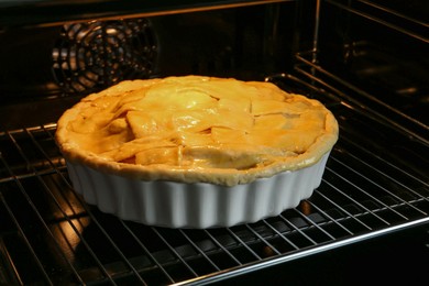 Photo of Baking dish with raw homemade apple pie in oven, closeup