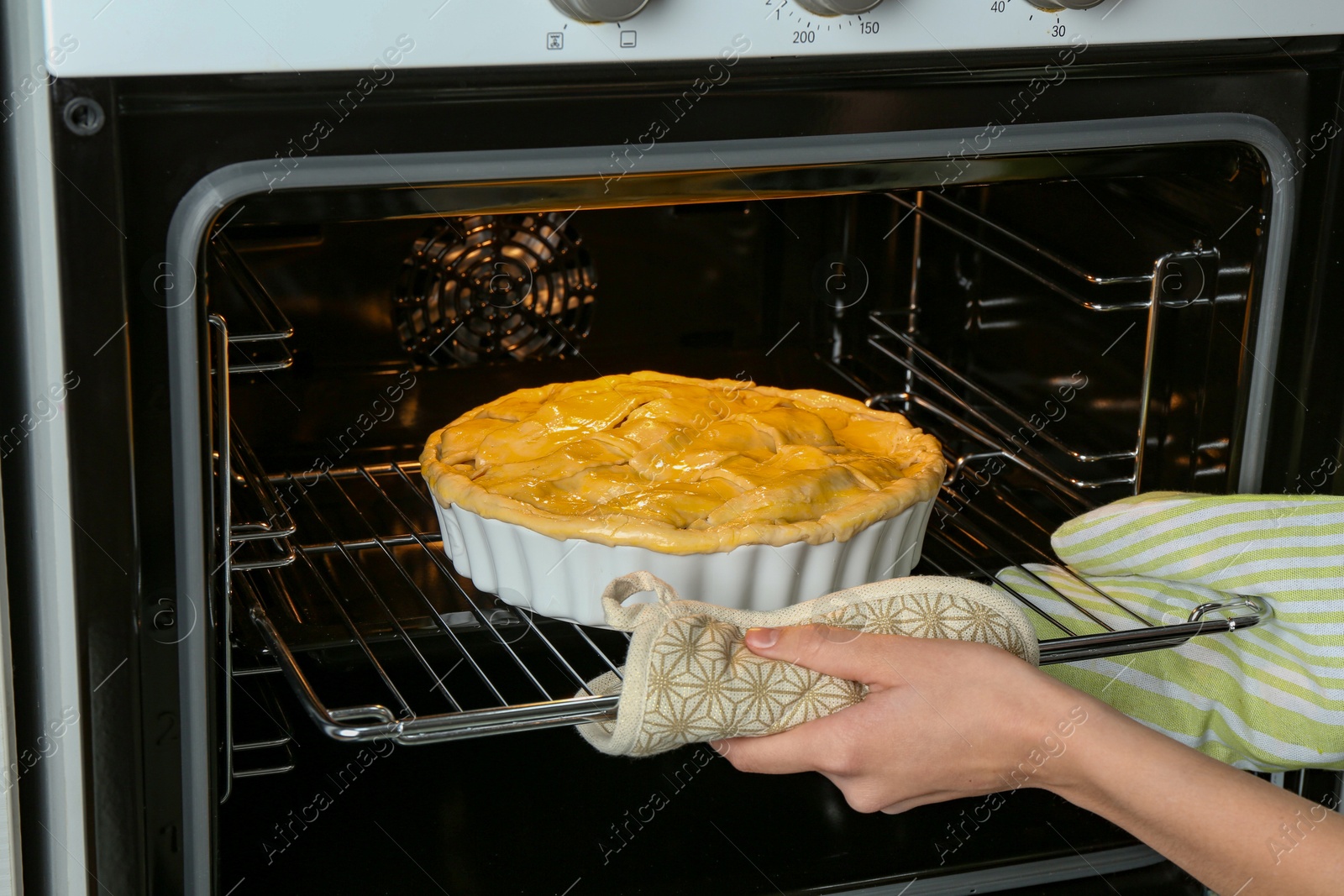 Photo of Woman putting homemade apple pie into oven in kitchen, closeup