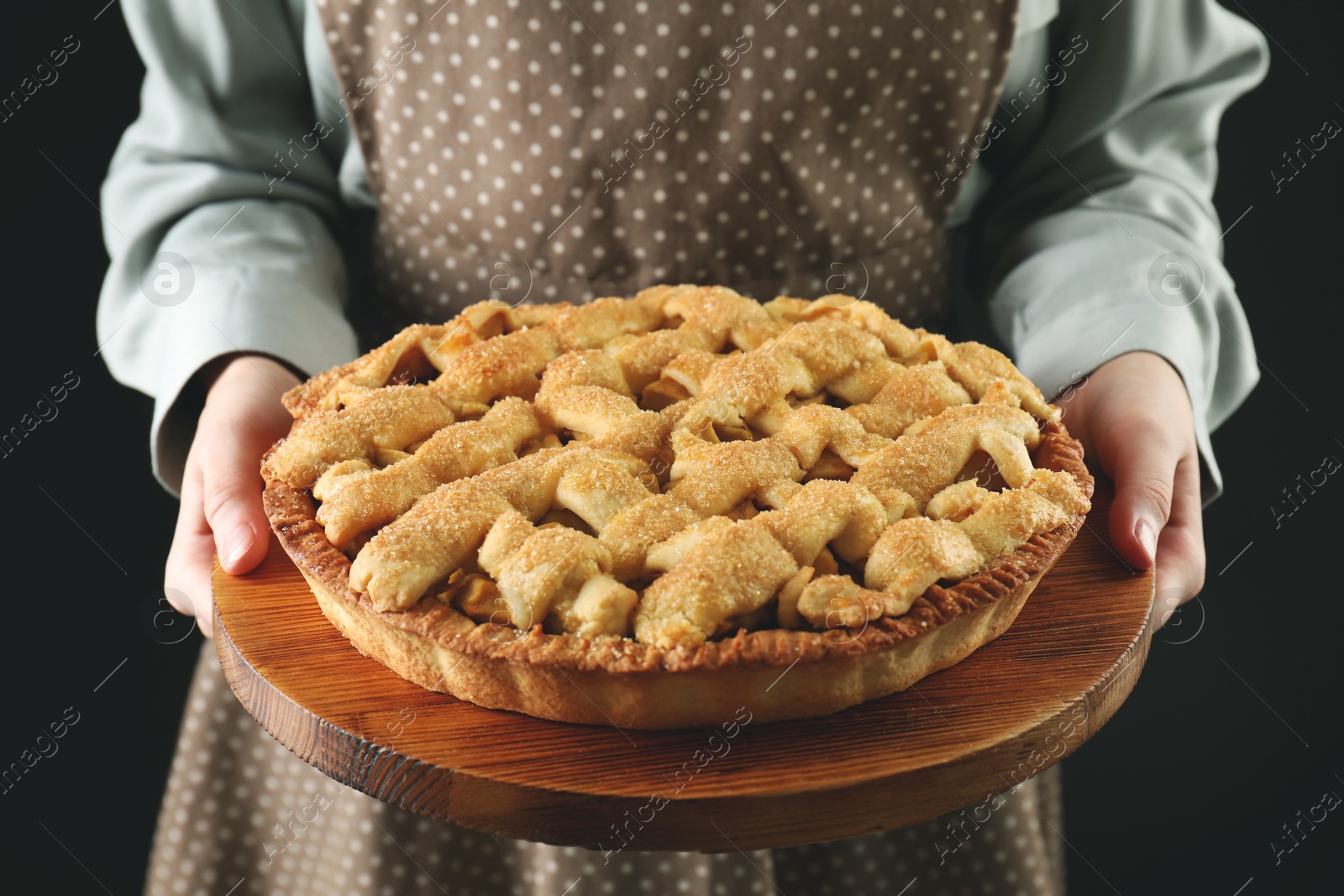 Photo of Woman holding wooden board with tasty homemade apple pie on black background, closeup