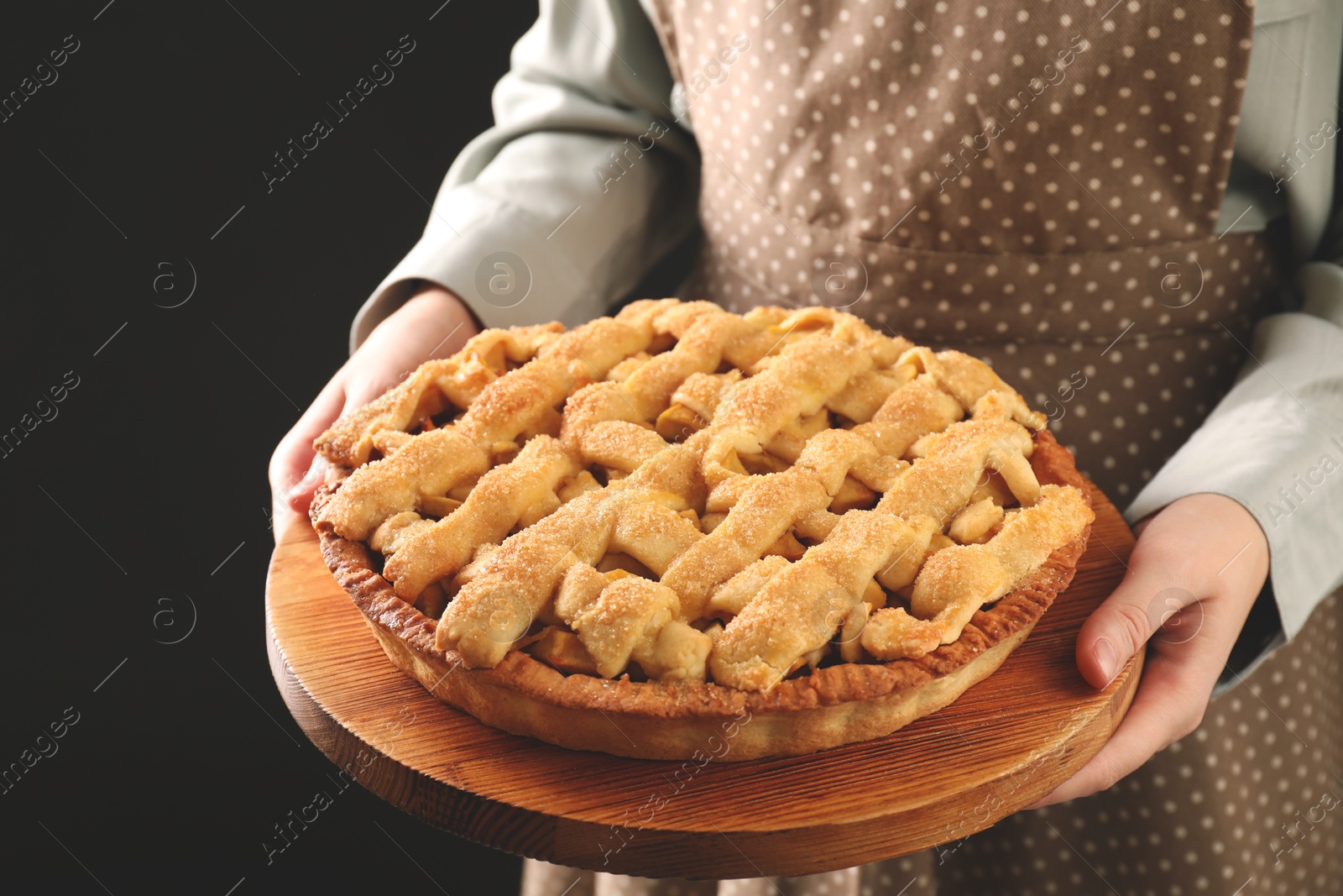 Photo of Woman holding wooden board with tasty homemade apple pie on black background, closeup