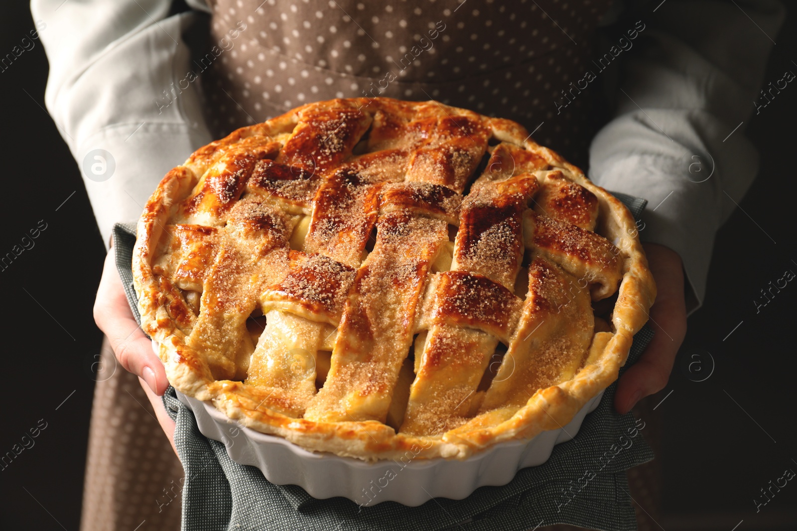 Photo of Woman holding tasty homemade apple pie on black background, closeup