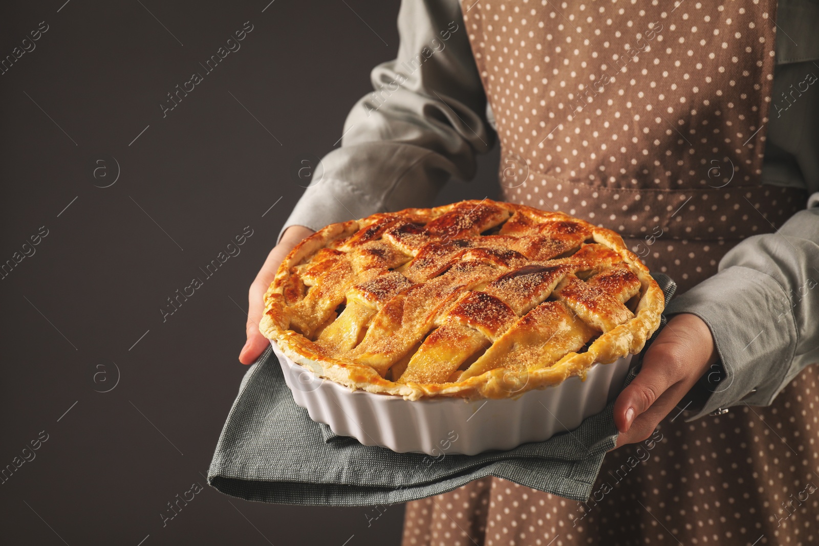 Photo of Woman holding tasty homemade apple pie on dark background, closeup. Space for text