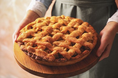 Photo of Woman holding wooden board with tasty homemade apple pie on light background, closeup