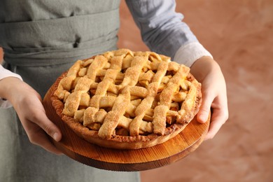 Photo of Woman holding wooden board with tasty homemade apple pie on light coral background, closeup