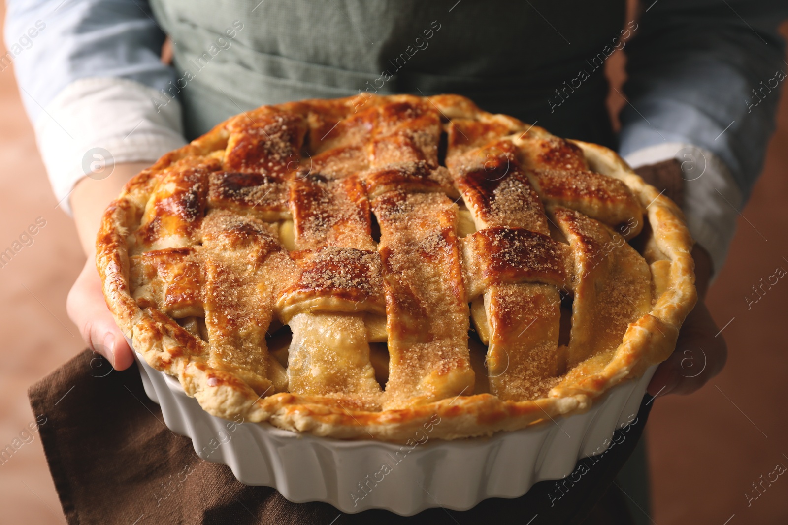 Photo of Woman holding tasty homemade apple pie on light coral background, closeup