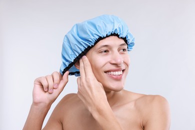 Photo of Happy man wearing shower cap on light grey background