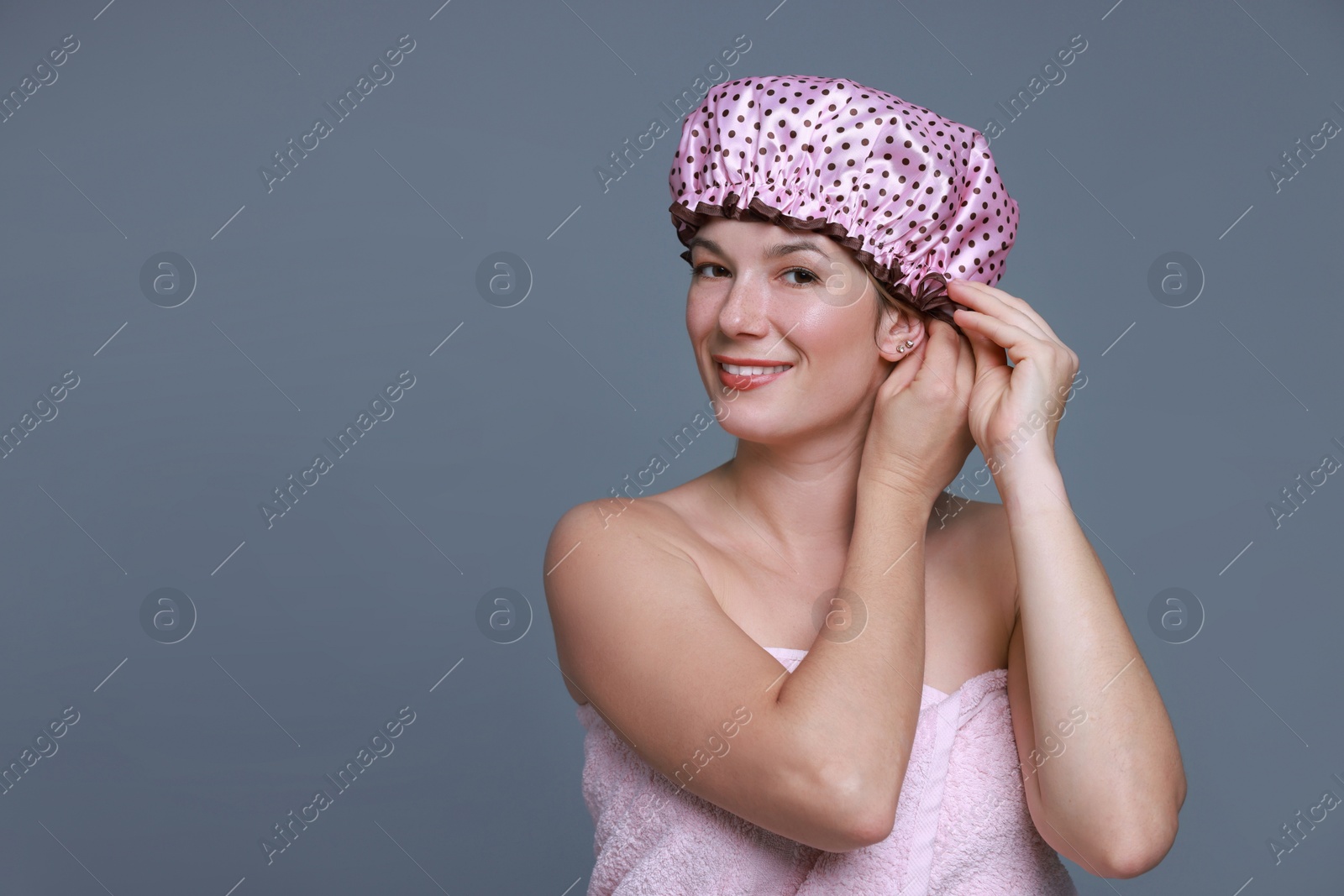 Photo of Happy woman wearing shower cap on grey background, space for text