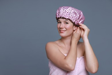 Happy woman wearing shower cap on grey background, space for text