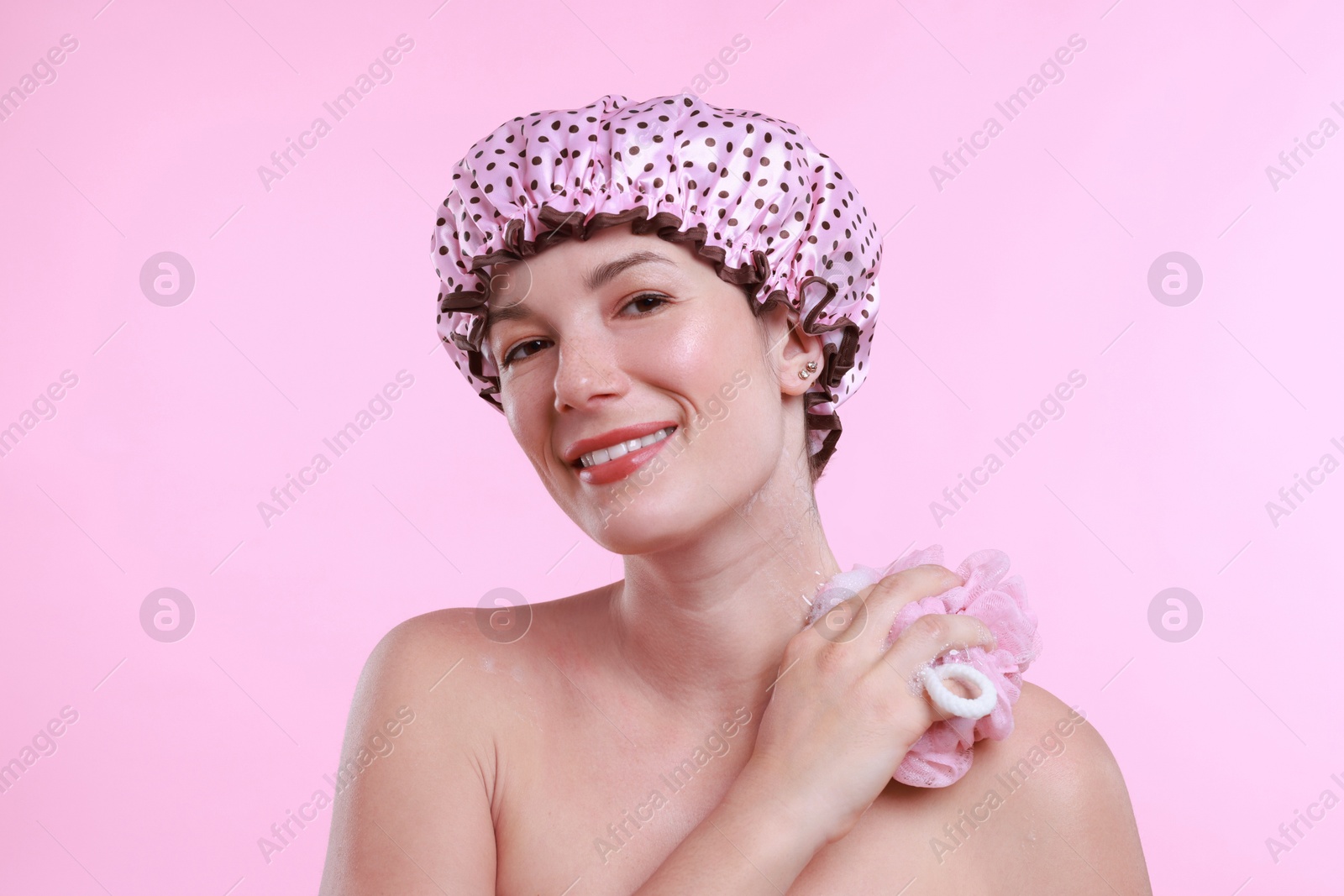 Photo of Woman with shower cap and mesh sponge on pink background