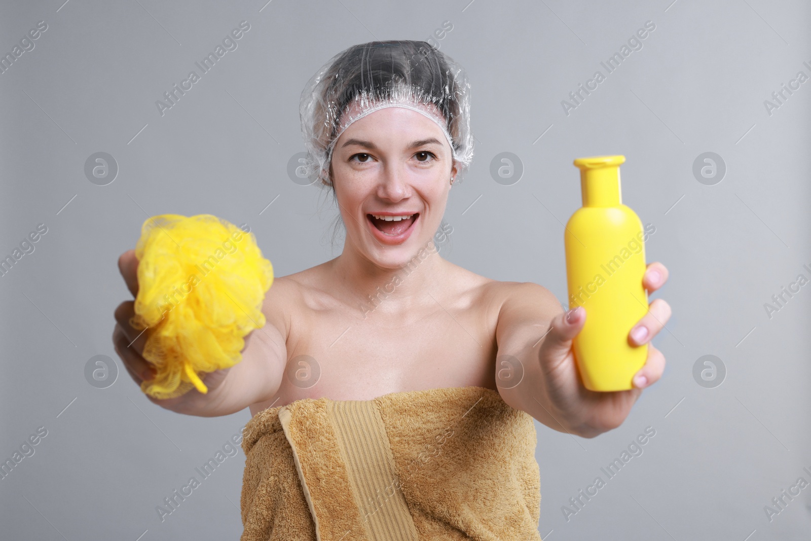 Photo of Woman with shower cap, shampoo and mesh sponge on grey background