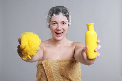 Photo of Woman with shower cap, shampoo and mesh sponge on grey background