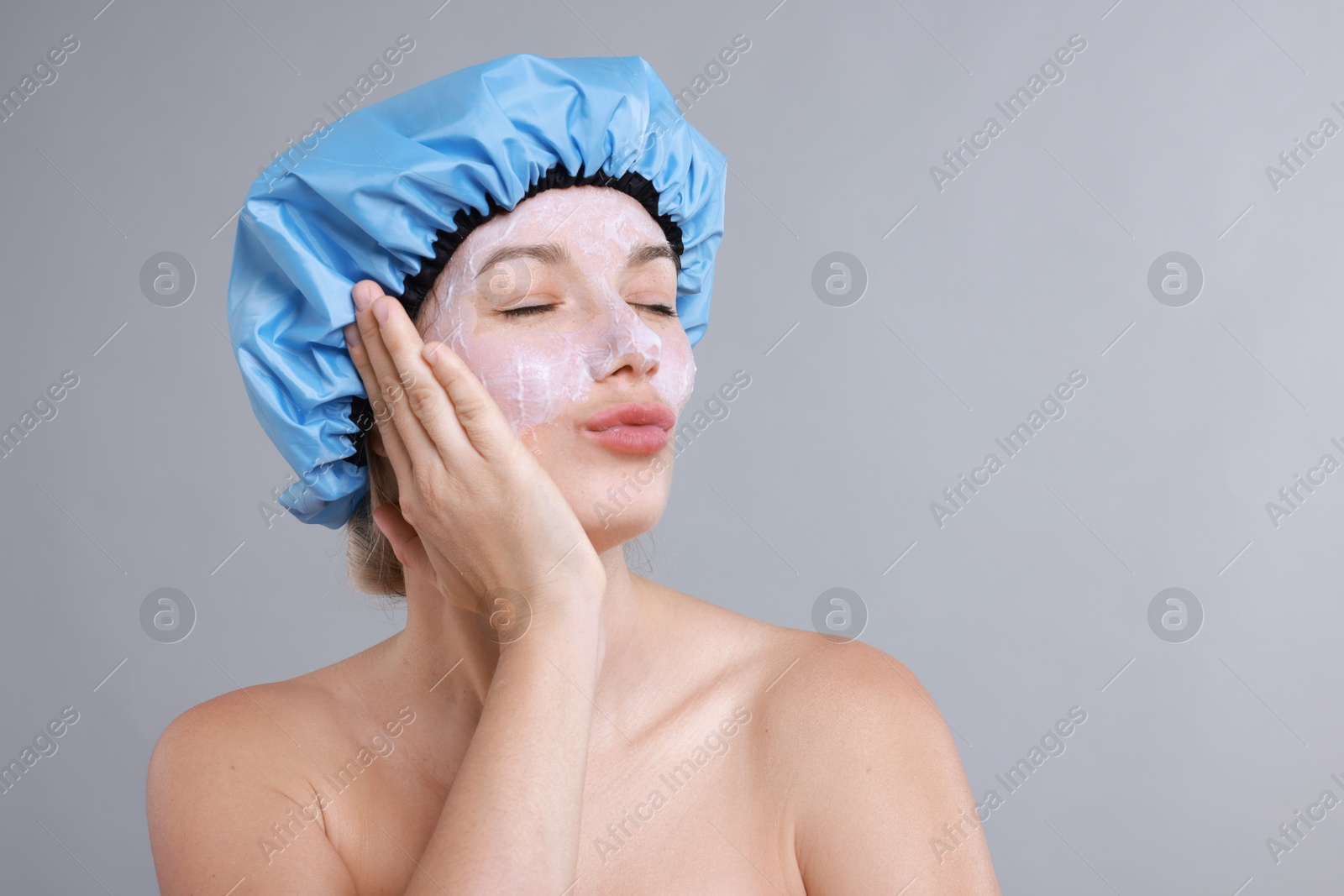 Photo of Woman with shower cap and cream on her face against grey background