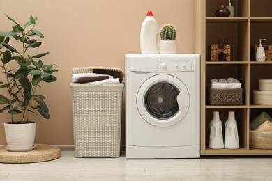 Photo of Wicker basket full of laundry, washing machine and detergent in bathroom