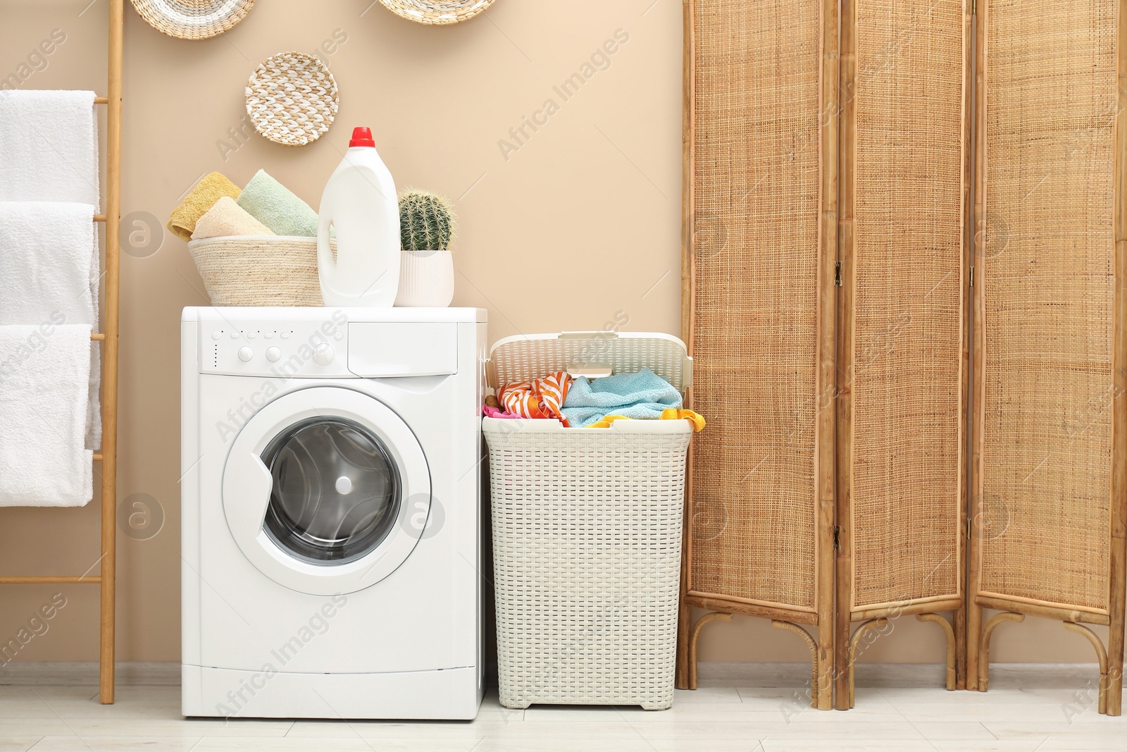 Photo of Wicker basket full of laundry, washing machine and detergent in bathroom