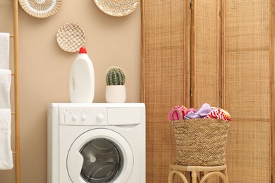 Photo of Wicker basket full of laundry, washing machine and detergent in bathroom