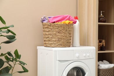 Photo of Wicker basket full of laundry, washing machine and detergent in bathroom