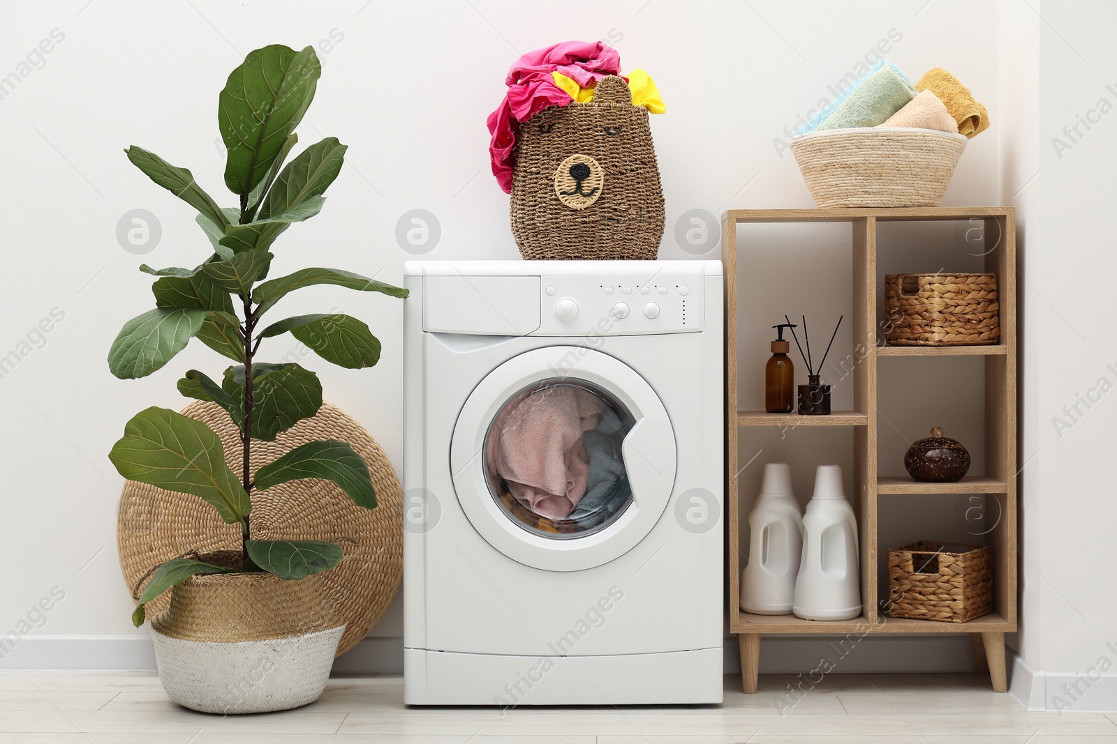 Photo of Wicker basket full of laundry, washing machine and detergents in bathroom