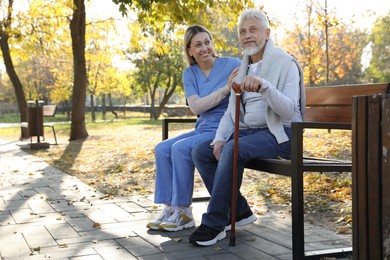 Photo of Caregiver assisting senior man on wooden bench in park, space for text. Home health care service