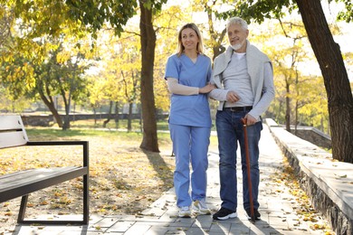 Photo of Caregiver assisting senior man in park, space for text. Home health care service