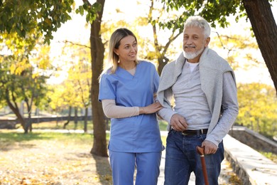 Photo of Caregiver assisting senior man in park. Home health care service