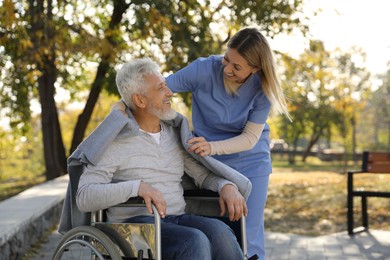 Photo of Caregiver assisting senior man on wheelchair in park. Home health care service