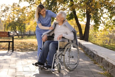 Photo of Caregiver assisting senior man on wheelchair in park. Home health care service