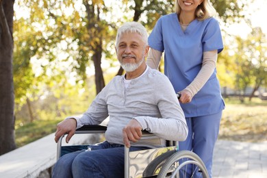 Photo of Caregiver assisting senior man on wheelchair in park. Home health care service