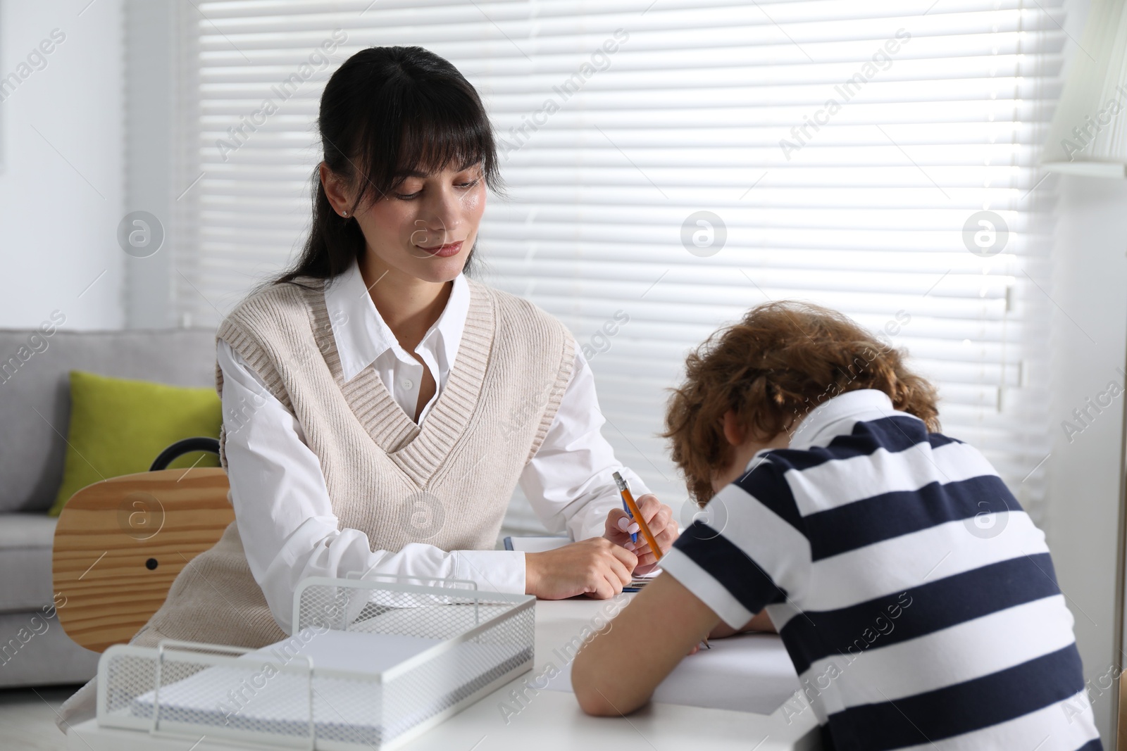 Photo of Little boy writing something at desk while psychologist taking notes