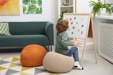 Little boy assembling letters on magnetic board indoors