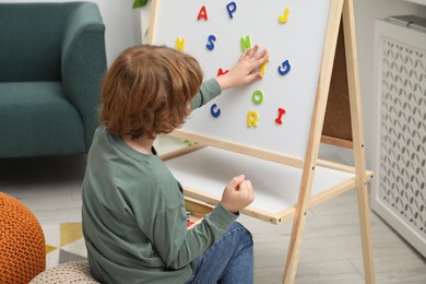 Little boy assembling letters on magnetic board indoors