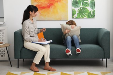 Upset little boy having therapy session with psychologist in office