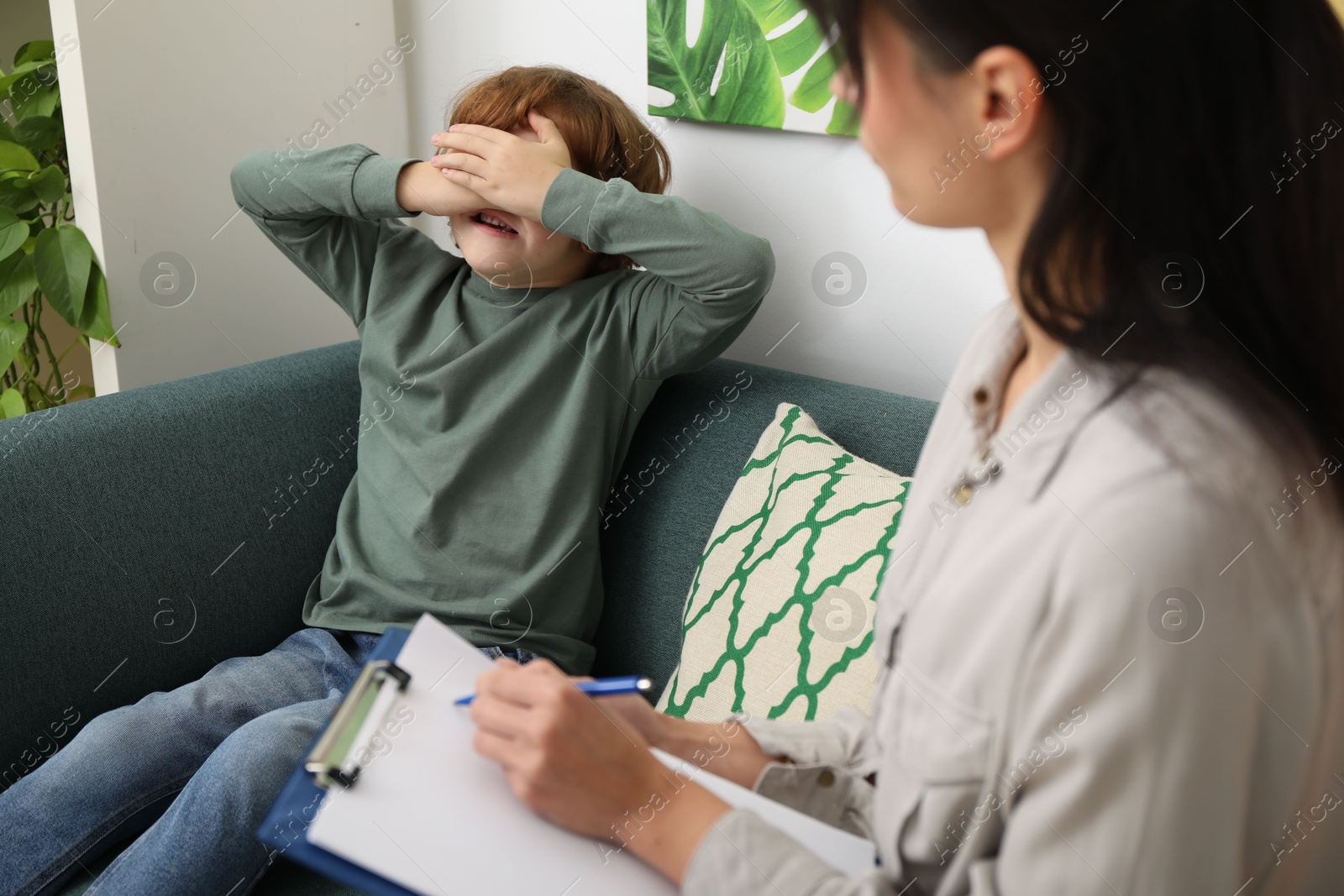 Photo of Upset little boy having therapy session with psychologist in office