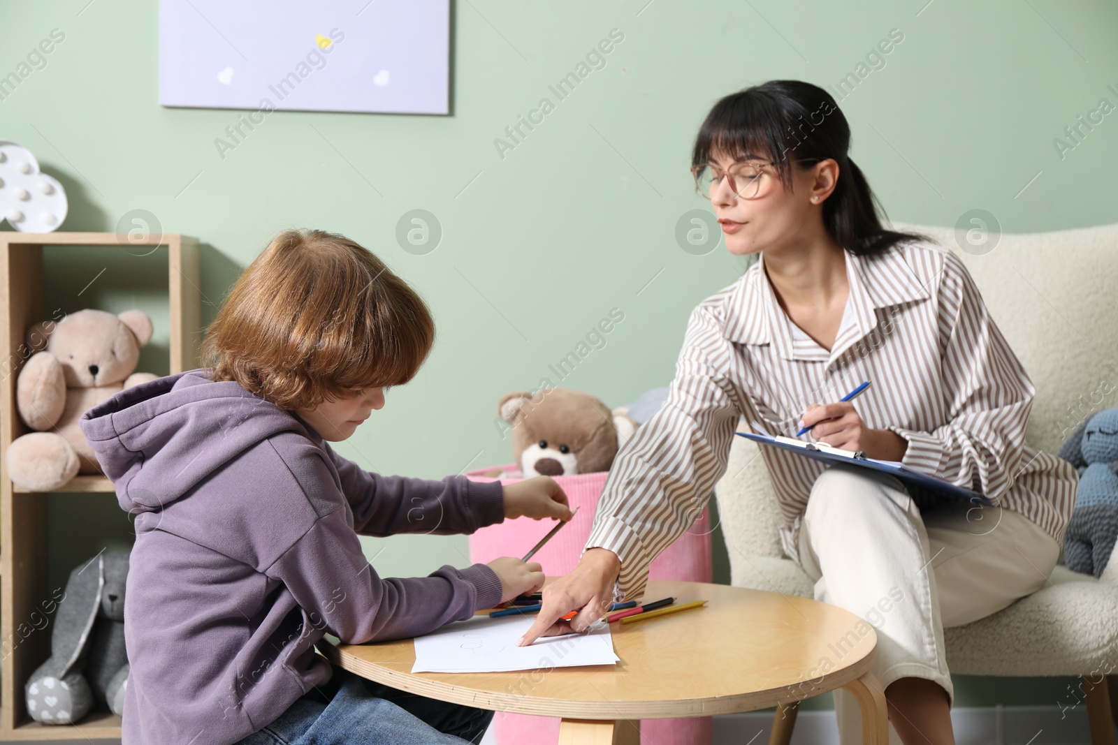 Photo of Boy drawing at table during consultation with psychologist indoors